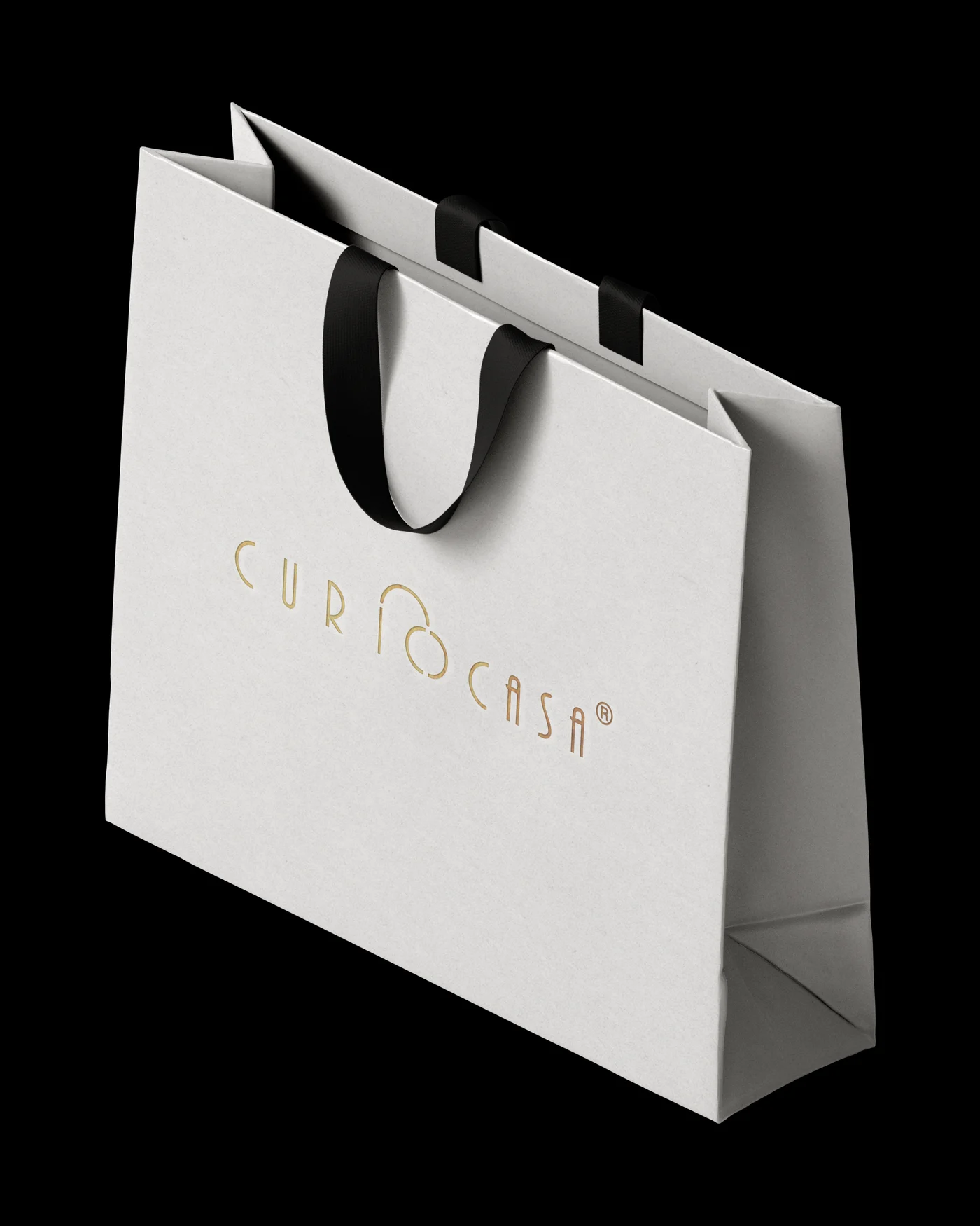 White Curiocasa shopping bag with a gold logo and black ribbon handles