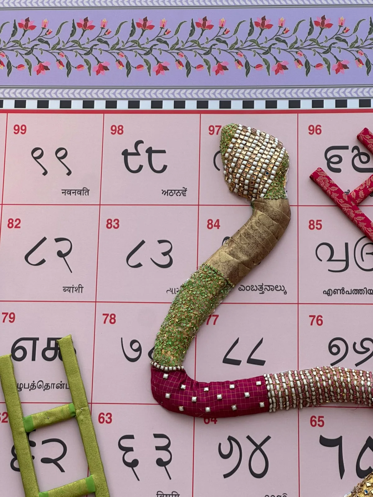 Close-up of a snake's head in green and gold beadwork, with a green ladder at the side.