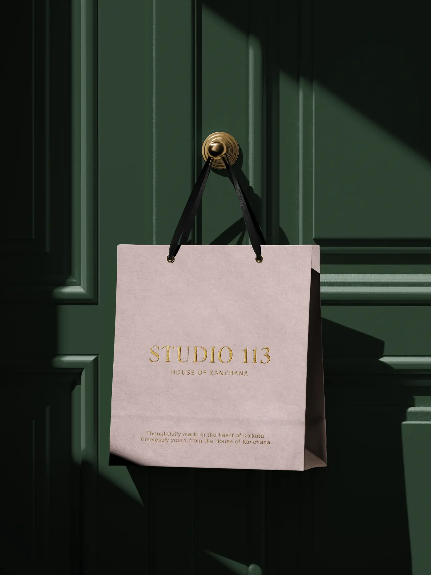 Blush Studio 113 shopping bag with gold foil, hanging from a brass door handle on a green door