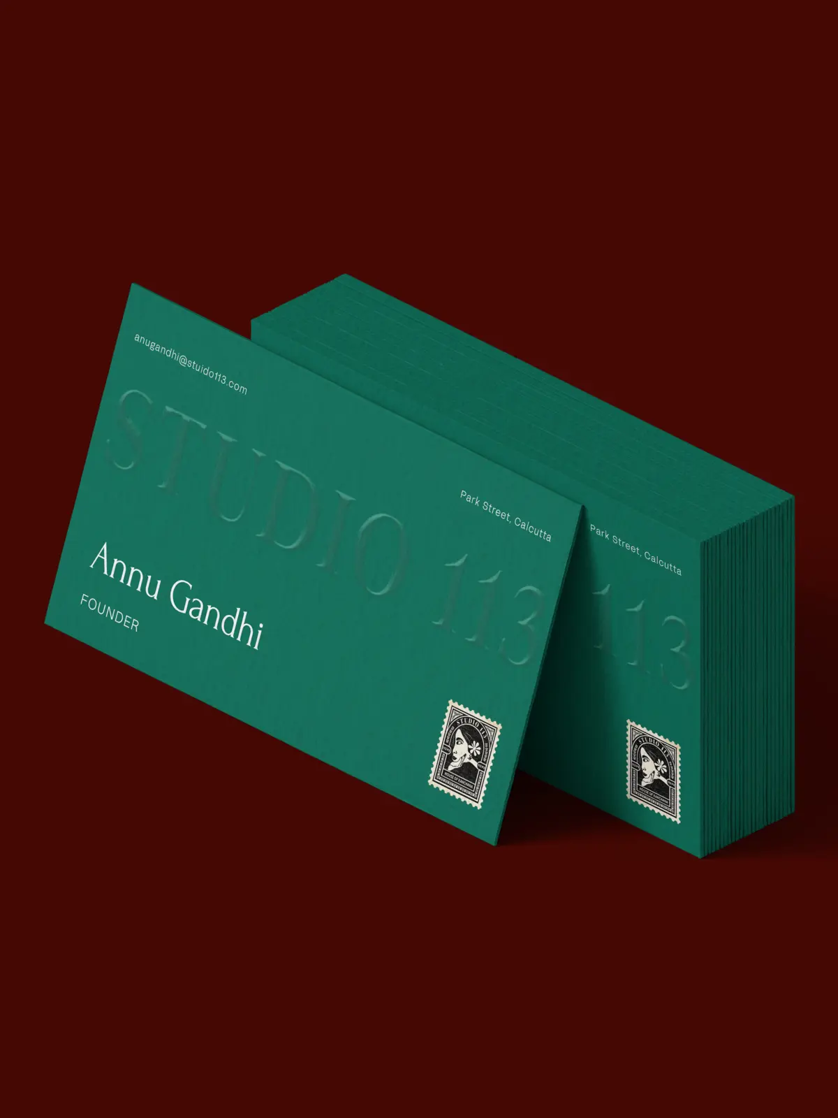Stack of green Studio 113 business cards with a blind-embossed wordmark and the stamp, on maroon