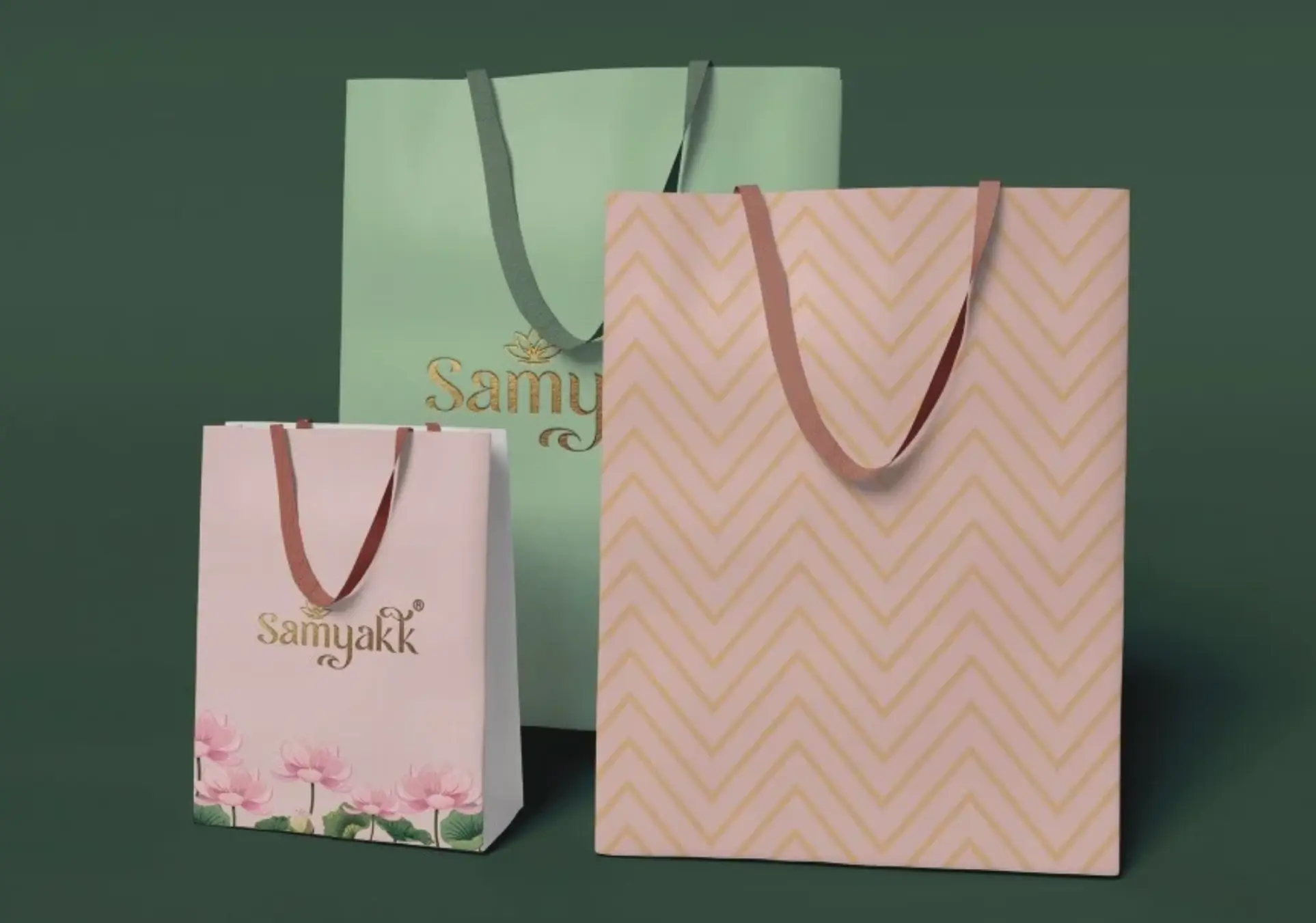 Samyakk paper bags: a celadon bag with the gold logo, a blush bag with lotuses and a blush chevron bag
