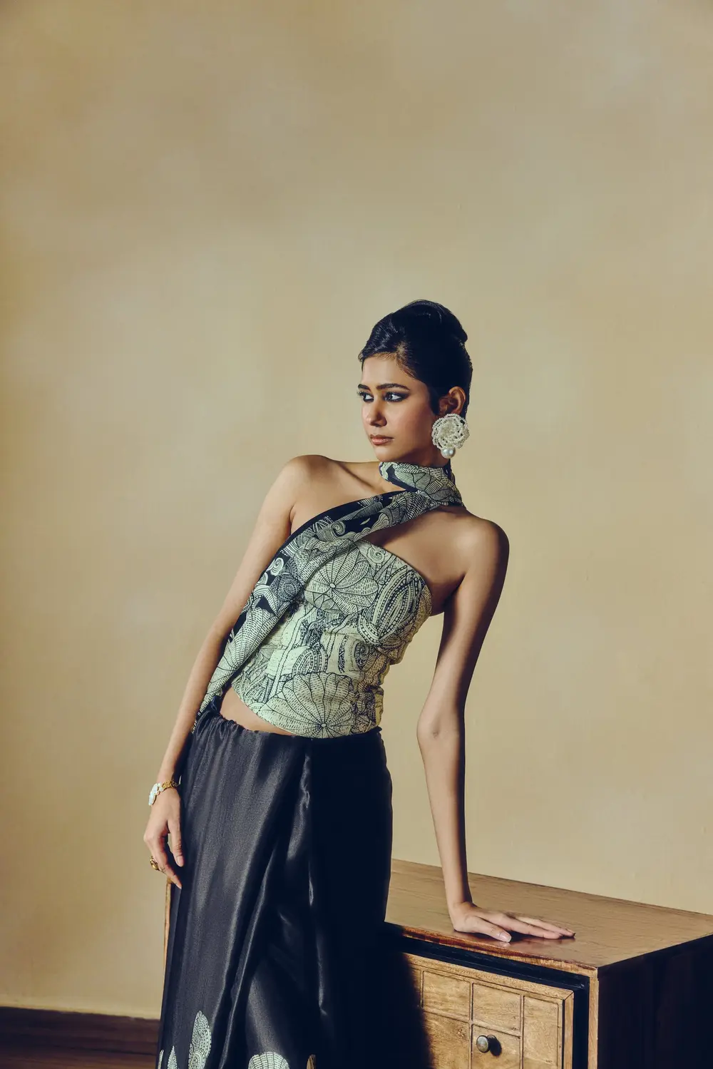 Model in a grey printed corset and black skirt, leaning on a wooden chest