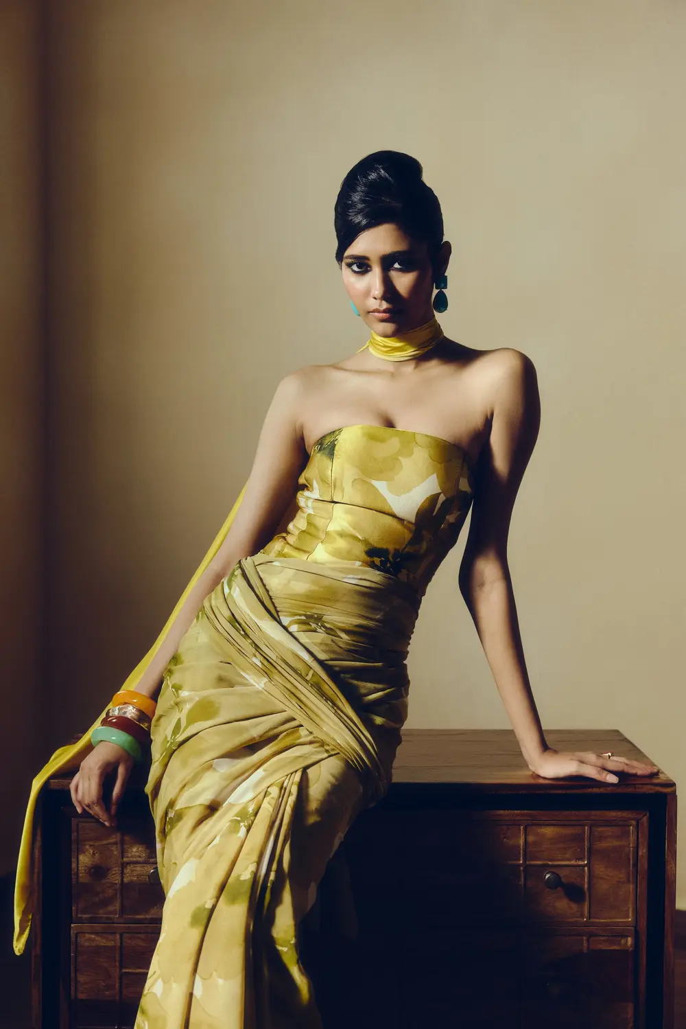 Model in an olive and mustard printed corset saree, seated on a wooden chest