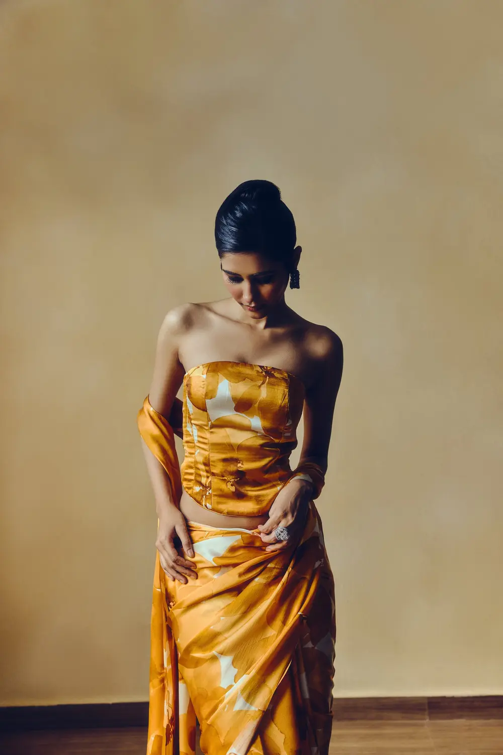 Model in a mustard printed corset with a draped skirt, looking down