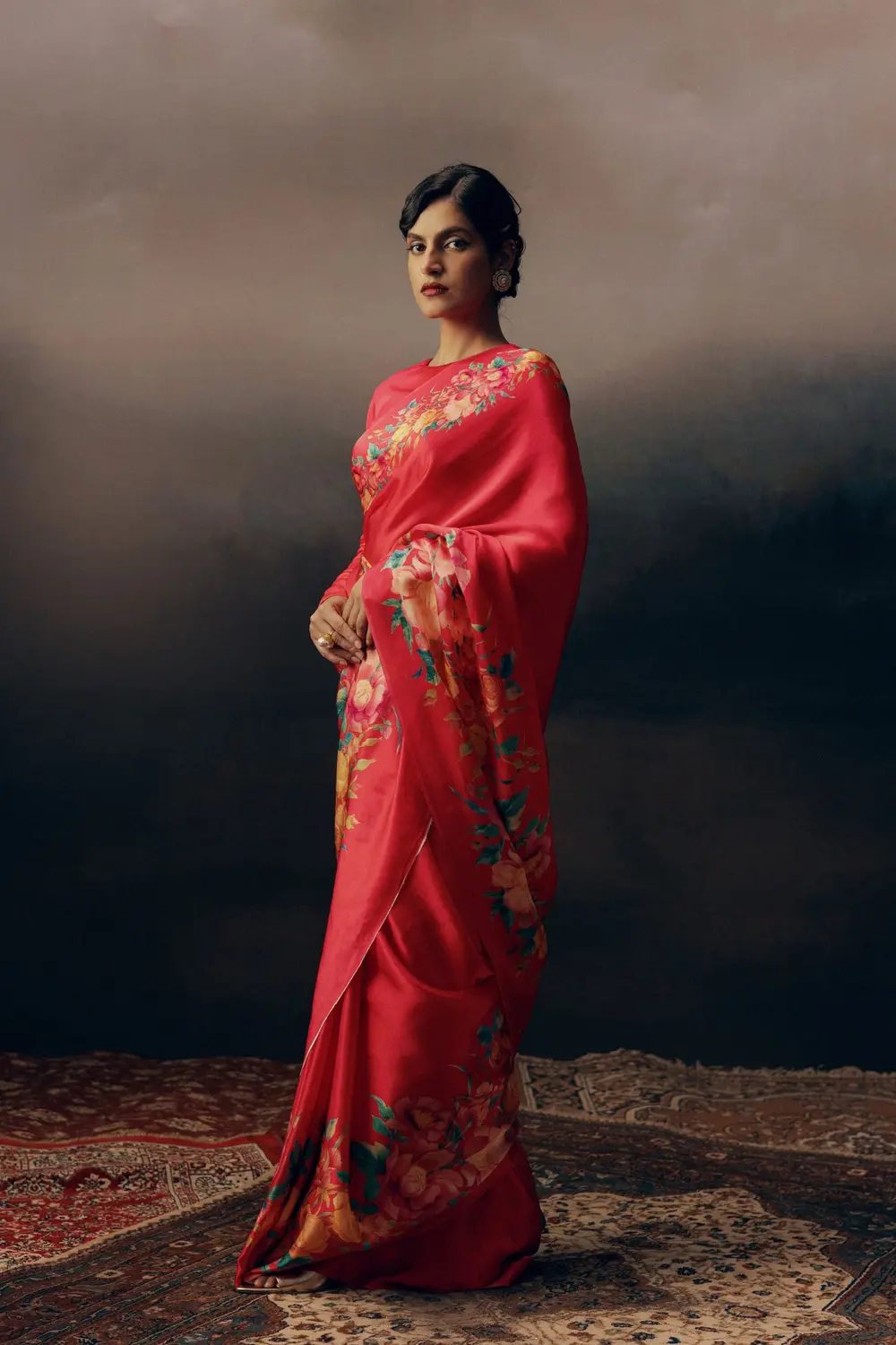 Model in a raspberry floral saree on a Persian rug against a dark painted sky