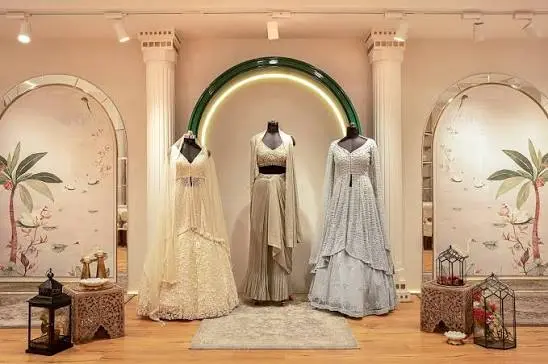 Three bridal lehengas under a banyan green arch lit in warm gold, between painted mural panels