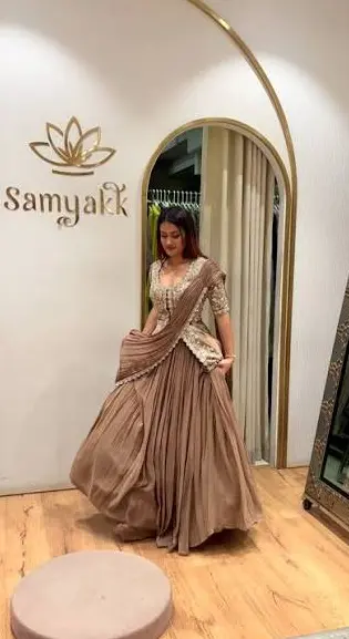 A bride in a draped lehenga beside the trial room arch, with the gold Samyakk wordmark on the wall