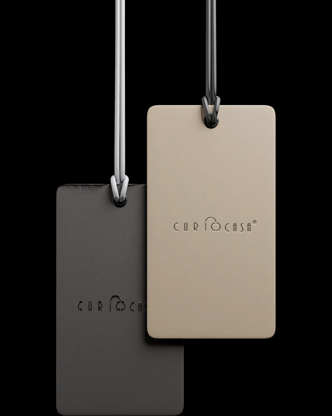 Two hanging Curiocasa tags, charcoal and sand, with debossed logos